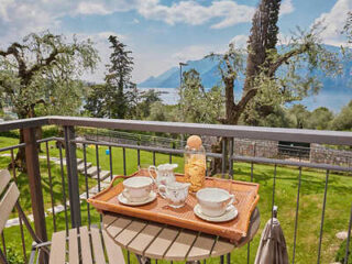 A tray with cups, saucers, and a bottle on a small balcony table. In the background, a scenic view of trees, mountains, and a lake.