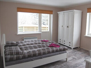 Bedroom with a white bed, gray plaid bedding, two pink towels on the bed, a large white wardrobe, and windows with a view of a snowy outdoor area.