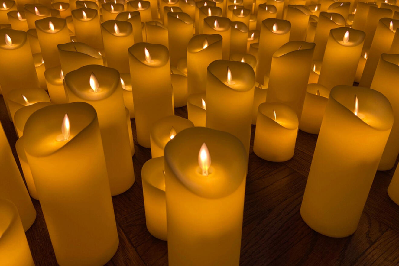 A close-up view of numerous lit candles arranged closely together on a wooden surface, creating a warm and inviting ambiance.