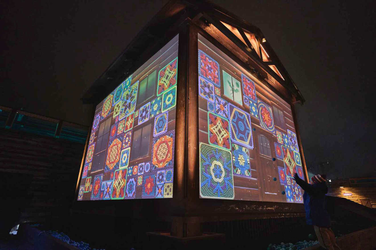 A person interacts with a large, illuminated cube displaying colorful geometric patterns in a nighttime setting.