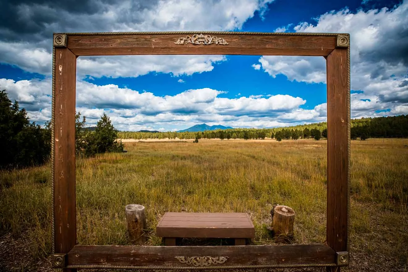 A large wooden frame set in a grassy landscape, with mountains and a blue sky in the background.