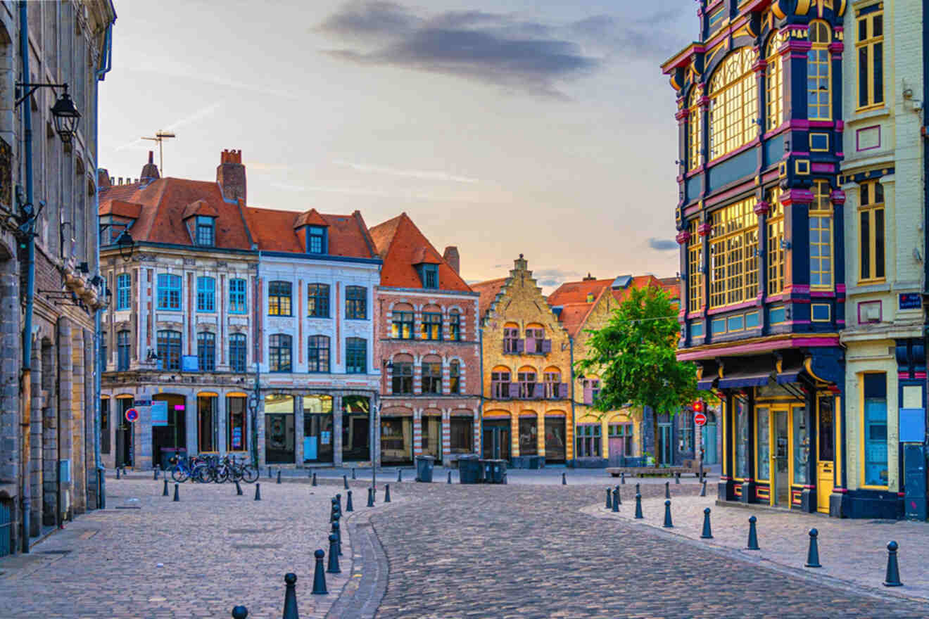 A cobblestone street lined with colorful, historic buildings and a vibrant cafe, under a partly cloudy sky at sunset.