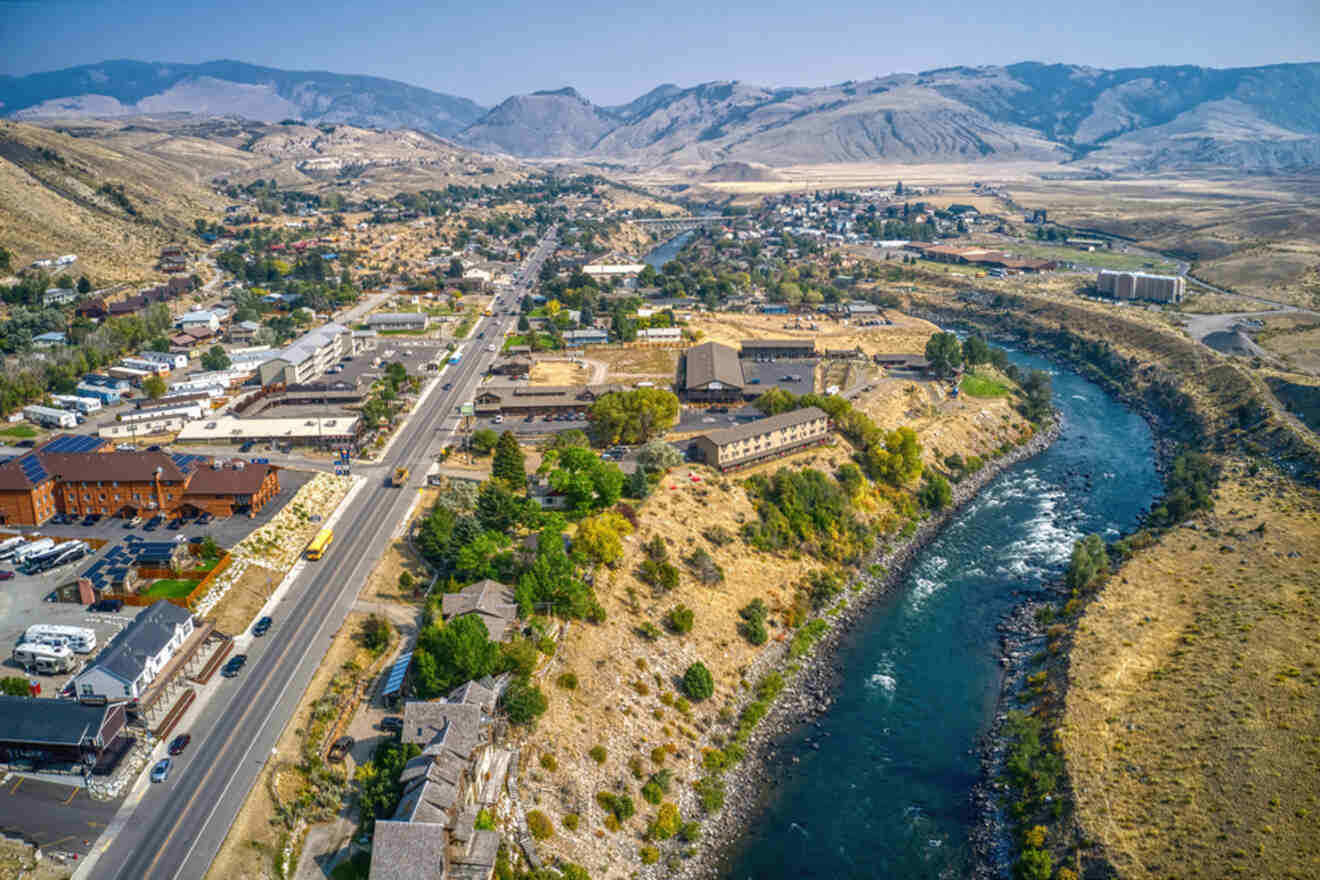 Aerial view of a small town beside a winding river, surrounded by arid hills and distant mountains. Roads, buildings, and greenery are visible.