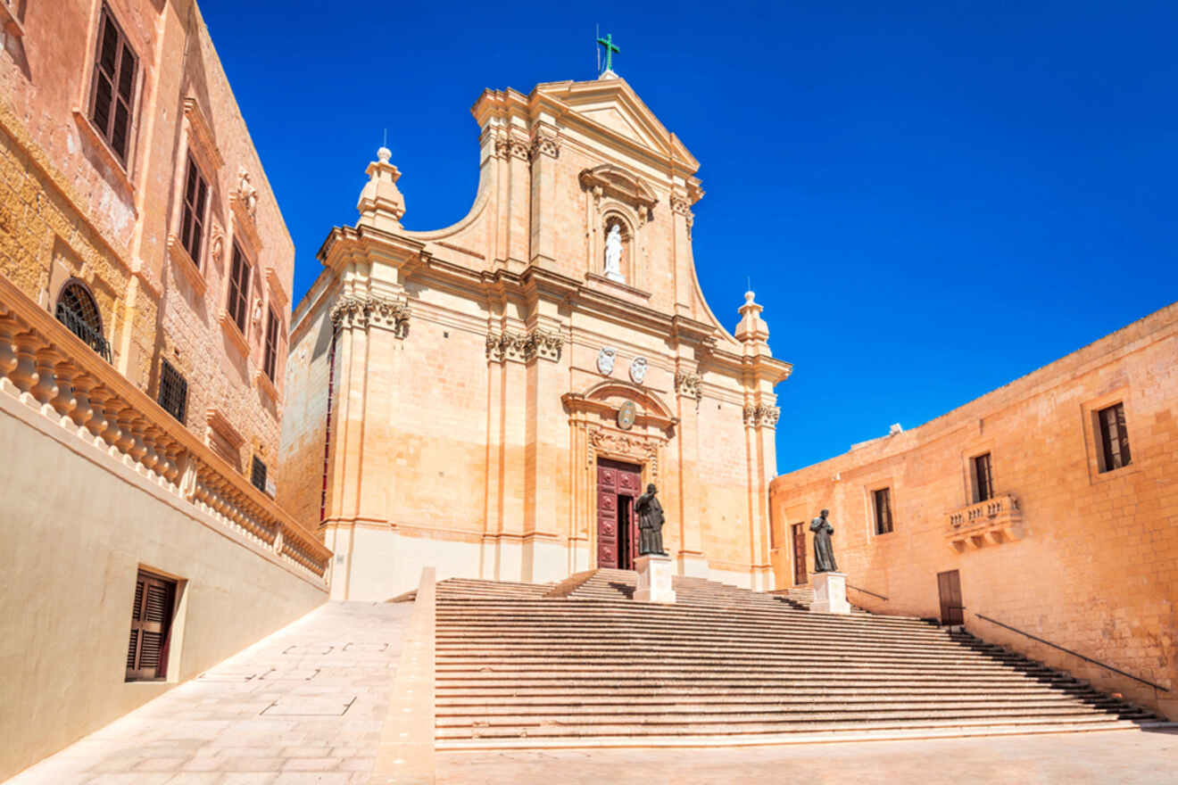 Baroque-style church with grand staircase, flanked by statues, under a clear blue sky.