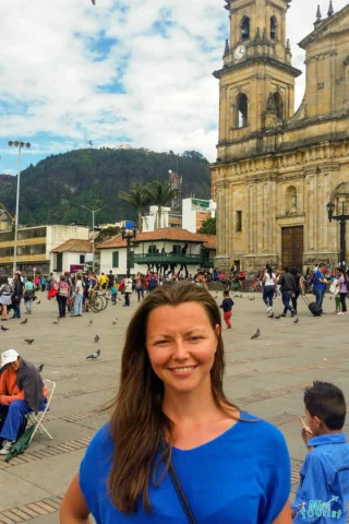 the author of the post in a blue shirt stands in a busy plaza with pigeons and a large church building in the background.