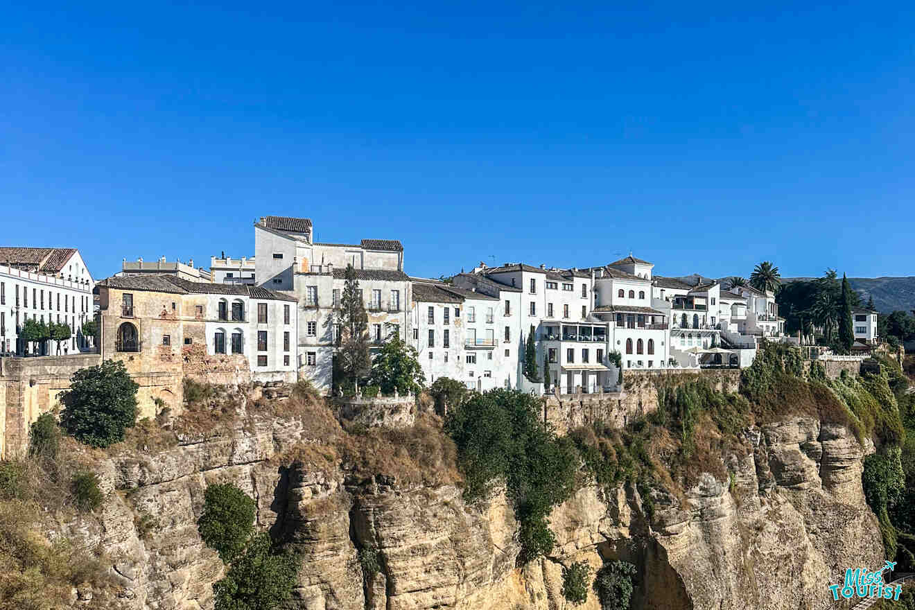 White houses perched on a cliff under a clear blue sky in Ronda, Spain.