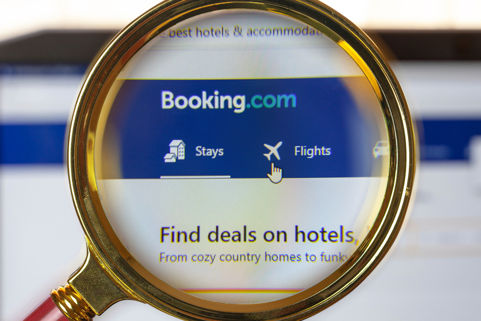 Magnifying glass focusing on Booking.com website, highlighting the "Stays" and "Flights" menu options. Cursor pointing to "Flights.