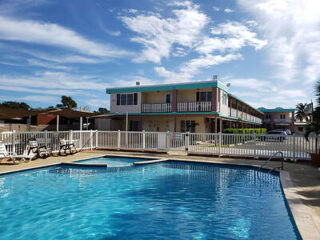 Outdoor swimming pool with lounge chairs next to a two-story building under a blue sky with clouds.