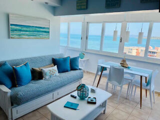 Bright living room with ocean view, blue and white decor, sofa with blue cushions, coffee table, and dining table near large windows.