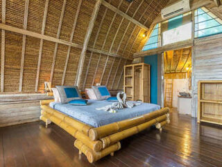 A bamboo-themed bedroom with a high, thatched ceiling features a bed, two blue pillows, and towel swans.