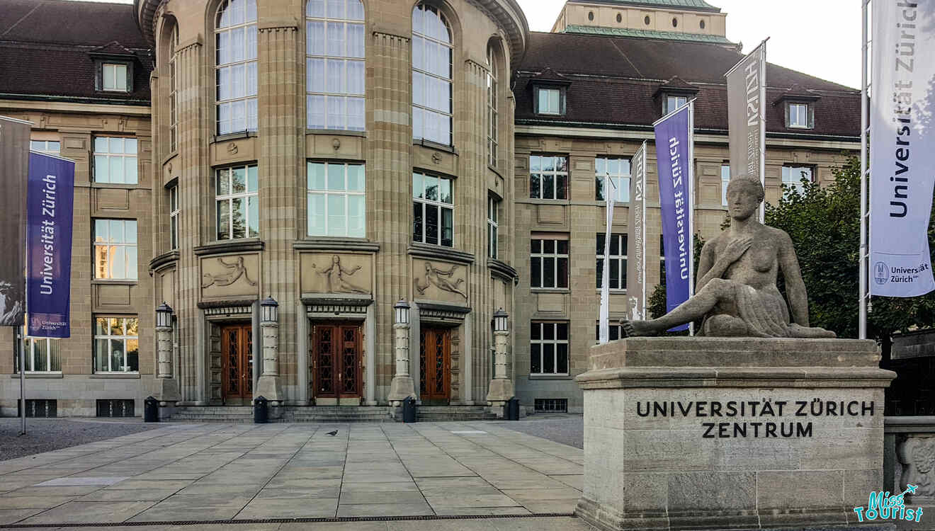 Entrance of Universität Zürich with a seated statue in front, banners on both sides, and a historic building facade in the background.