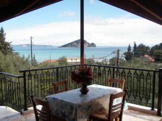 A balcony with a table and chairs overlooks a scenic view of the sea and a small island in the distance.