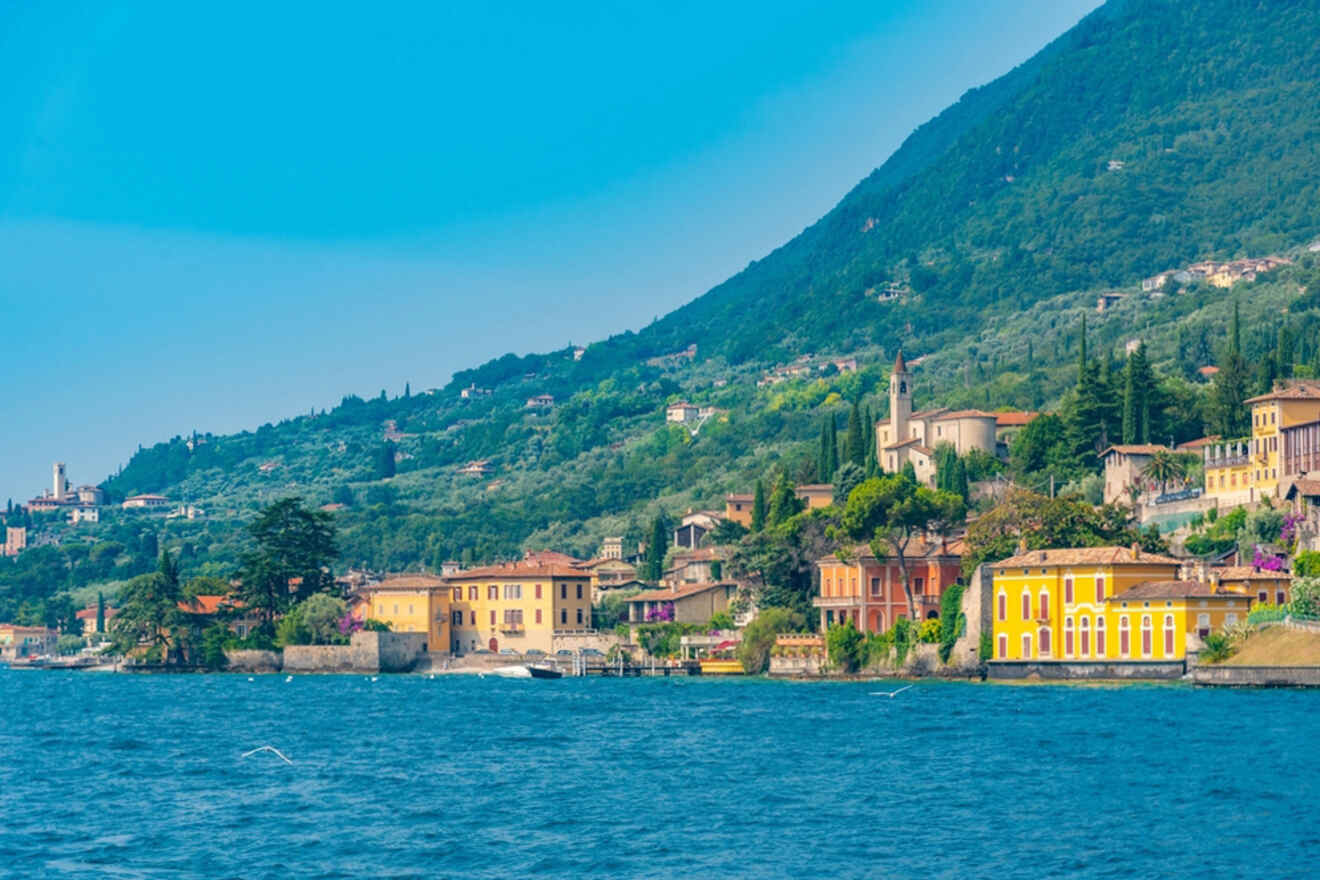 Scenic view of a lakeside village with colorful buildings, lush green hills, and a clear blue sky.