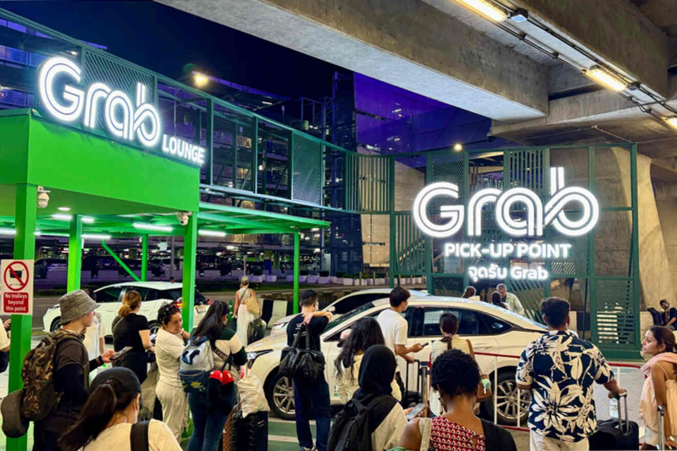 People waiting at a Grab pick-up point under a bridge, with cars and illuminated signs in the background at night.