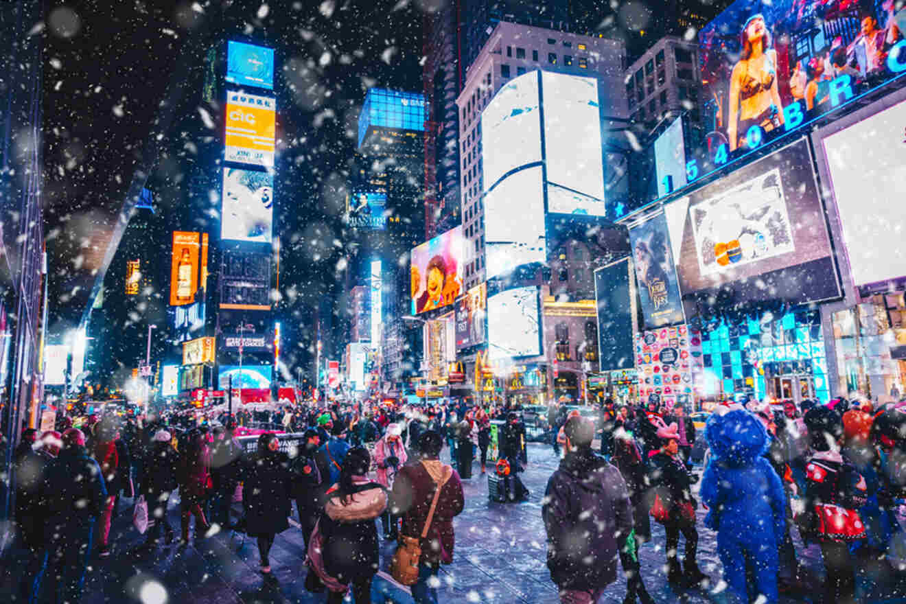 A bustling Times Square at night, with bright billboards illuminated and snow falling, while a crowd of people walk through the scene.