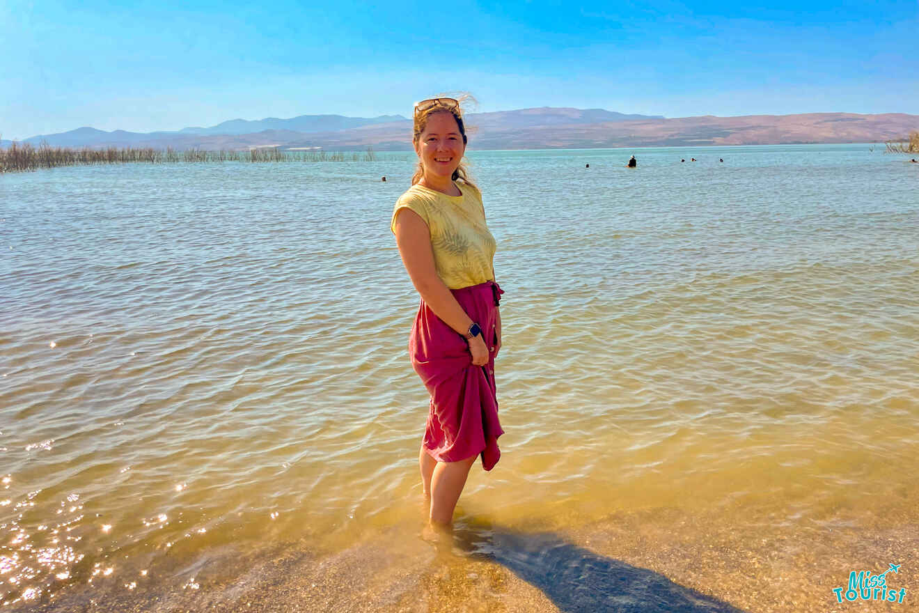 The writer of the post stands in shallow water at a lake, with mountains visible in the background. The sky is clear and sunny.