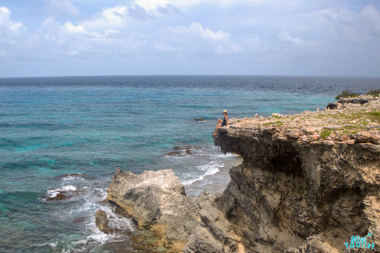 author of the post sits on the edge of a rocky cliff overlooking a vast ocean under a partly cloudy sky.