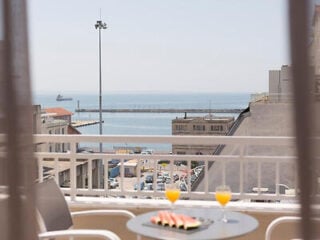 Shorter version under 125 characters: "Balcony table with watermelon and orange juice overlooking the Thessaloniki port at Plaza Hotel.