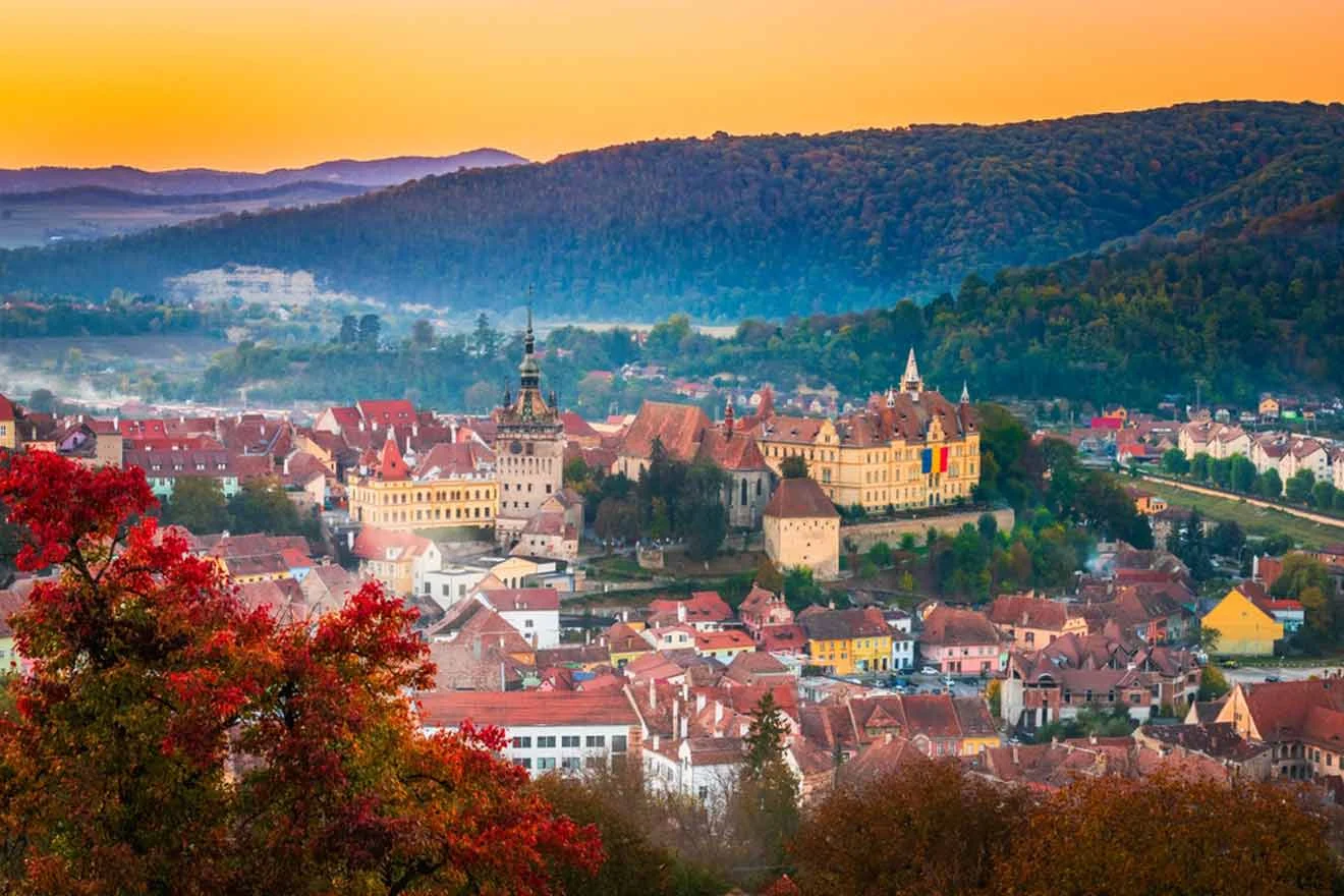 Scenic view of a historic town at sunset, surrounded by hills and autumn trees.