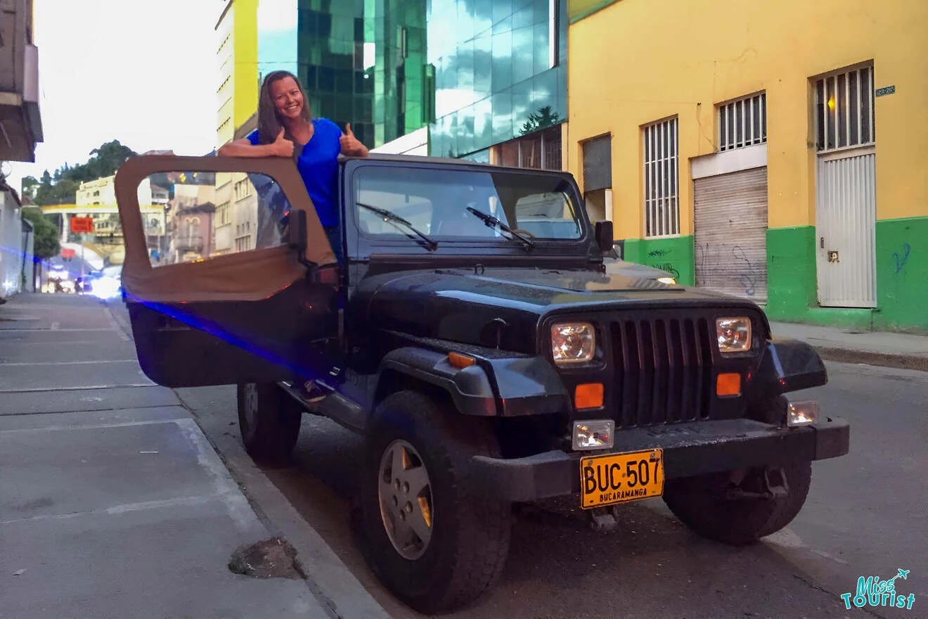 the author of the post poses next to a black Jeep with the door open on a city street, showing a thumbs-up gesture. Buildings are visible in the background.