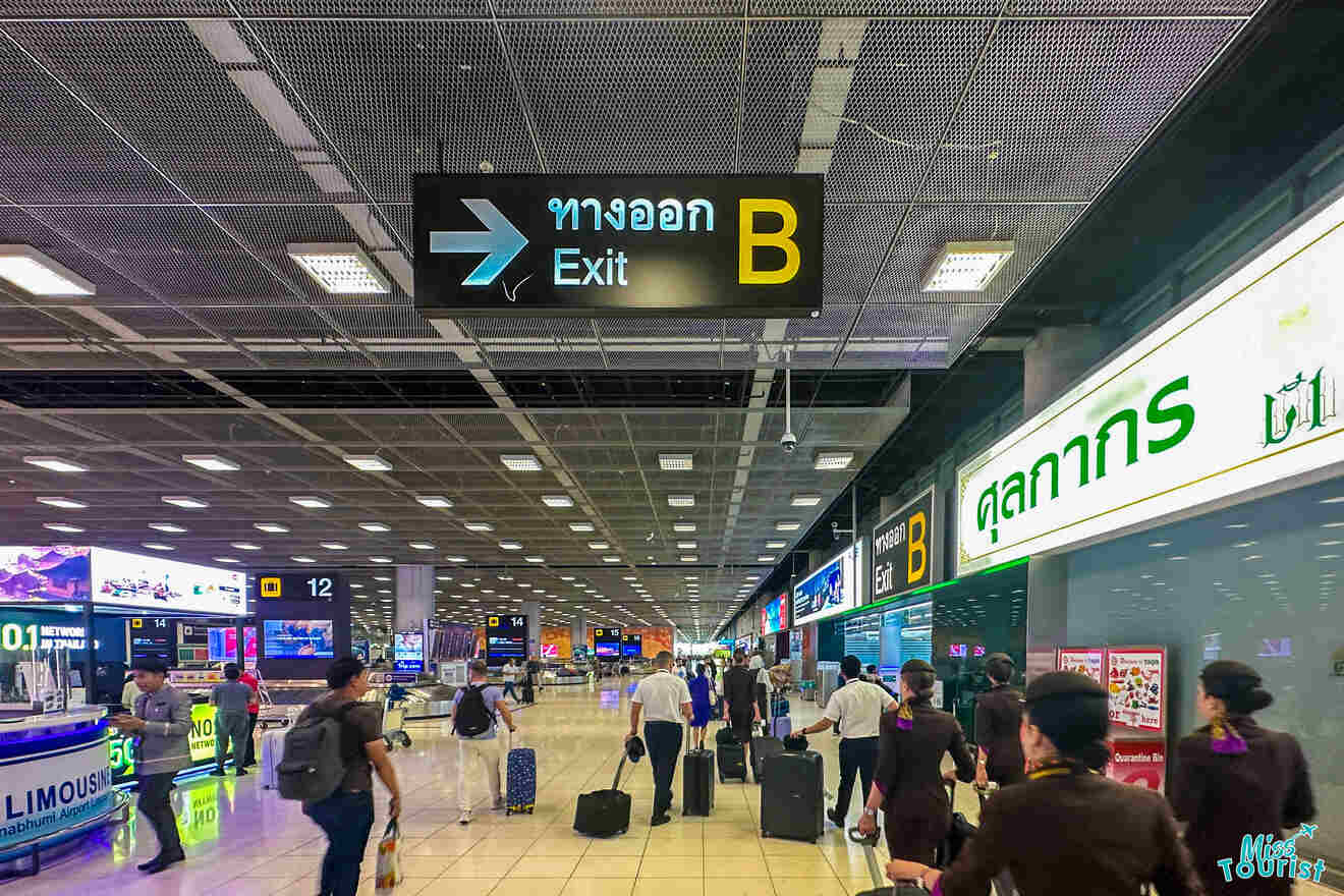 People walking with luggage in an airport terminal, following signs for Exit B.