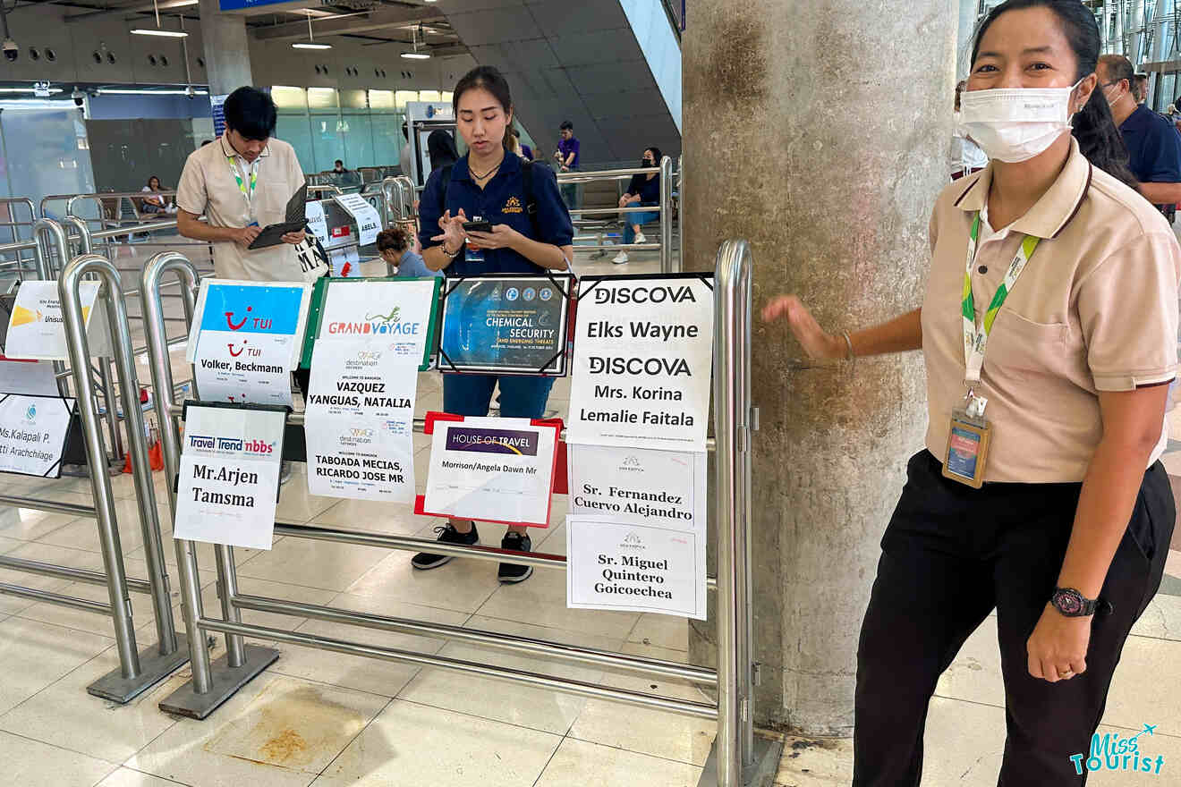 Two airport staff are standing near a row of signs displaying various names and greetings for arrivals.