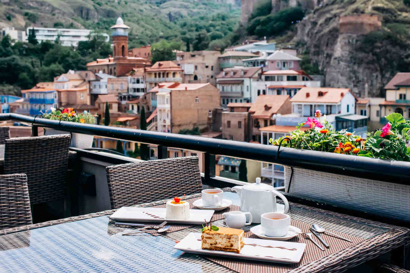 Outdoor cafe table with tea and desserts, overlooking a scenic view of colorful houses on a hillside.