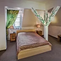 A bedroom with a bed, decorative pillows, two bedside tables with lamps, a window with green curtains, and a unique wall design with branching patterns.