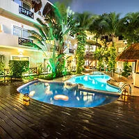 A tropical hotel courtyard features a uniquely shaped pool surrounded by lush greenery and lit up in the evening.