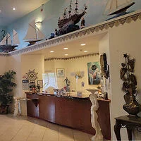 Lobby with nautical decor, featuring model ships on a shelf above a wooden reception desk. Walls adorned with maritime-themed art.