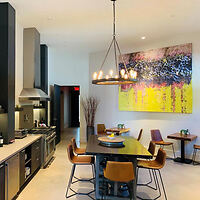 Modern kitchen and dining area with a large table, brown chairs, stainless steel appliances, and a colorful abstract painting on the wall.