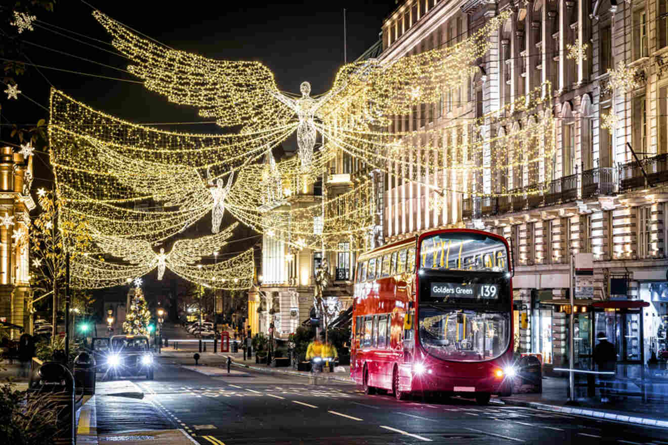 A red double-decker bus travels through a city street decorated with illuminated angel-shaped lights at night.