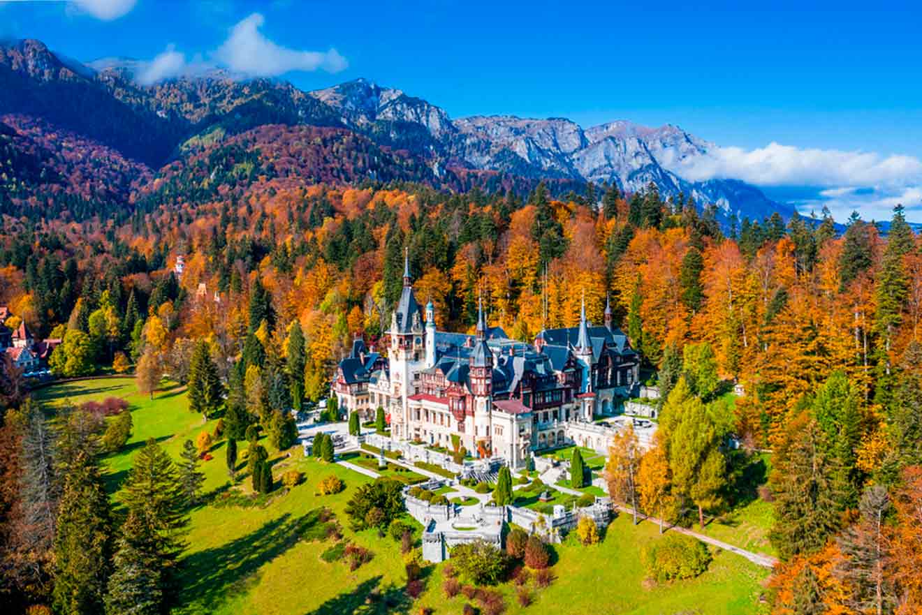 Castle surrounded by vibrant autumn trees and mountains under a clear blue sky.