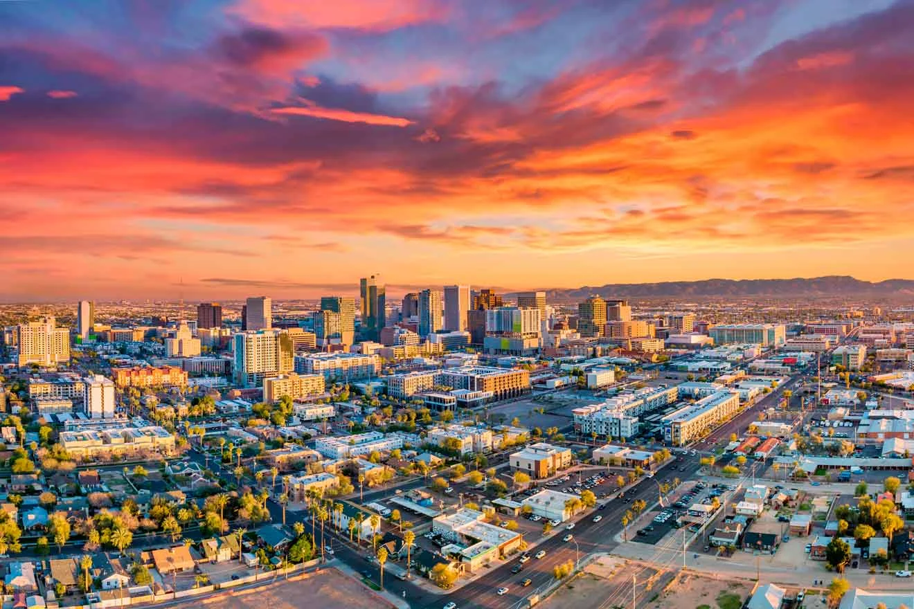 Aerial view of an urban cityscape at sunset, featuring a mix of buildings under a vibrant sky with orange and pink clouds.