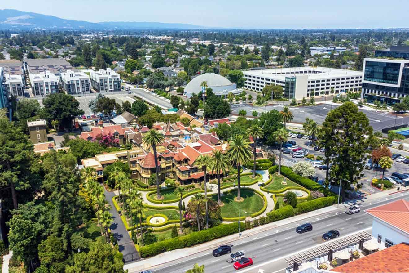 Aerial view of a large mansion surrounded by gardens and trees, set in an urban area with nearby office buildings and a parking lot.