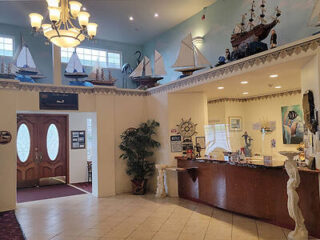 Lobby area with nautical-themed decor, including model ships and a ship wheel. Reception desk in the corner, with a chandelier above and double doors leading outside.