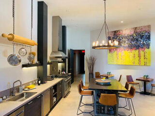 Modern kitchen with a large dining table, hanging light fixture, stainless steel appliances, and a colorful abstract painting on the wall.