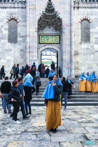 People gather at the entrance of the Blue Mosque in Istanbul. author of the post in a yellow skirt and blue headscarf stands in the foreground.