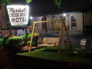 A lit sign reads "Marshalls Creek Rest Motel" beside a wooden swing and chairs. The building is visible in the background at night.