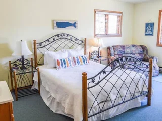 A bedroom with a metal-framed bed, white bedding, two side tables with lamps, a floral couch, a small dresser, and two wall decorations.