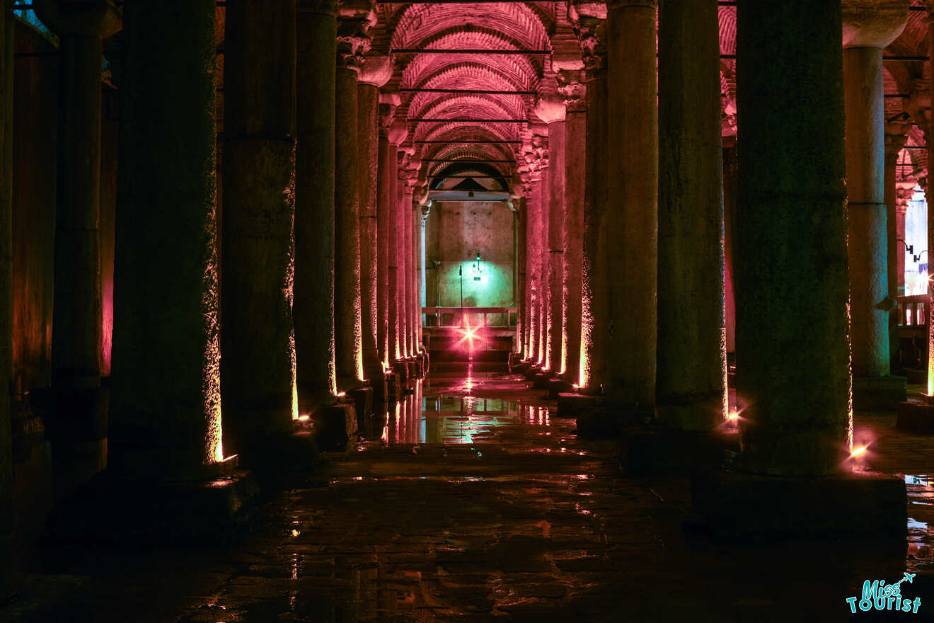 Interior of a dimly lit, pink-illuminated ancient underground cistern with rows of columns reflected in the water on the floor.