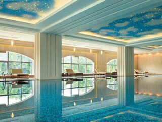 Indoor pool with a reflective ceiling painted with clouds and stars. Several lounge chairs line the windows, offering a view of greenery outside.