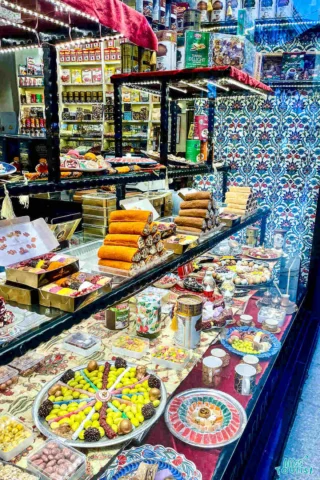 A colorful Turkish delight and dessert shop display with various sweets, candies, and packaged goods on shelves and a counter.