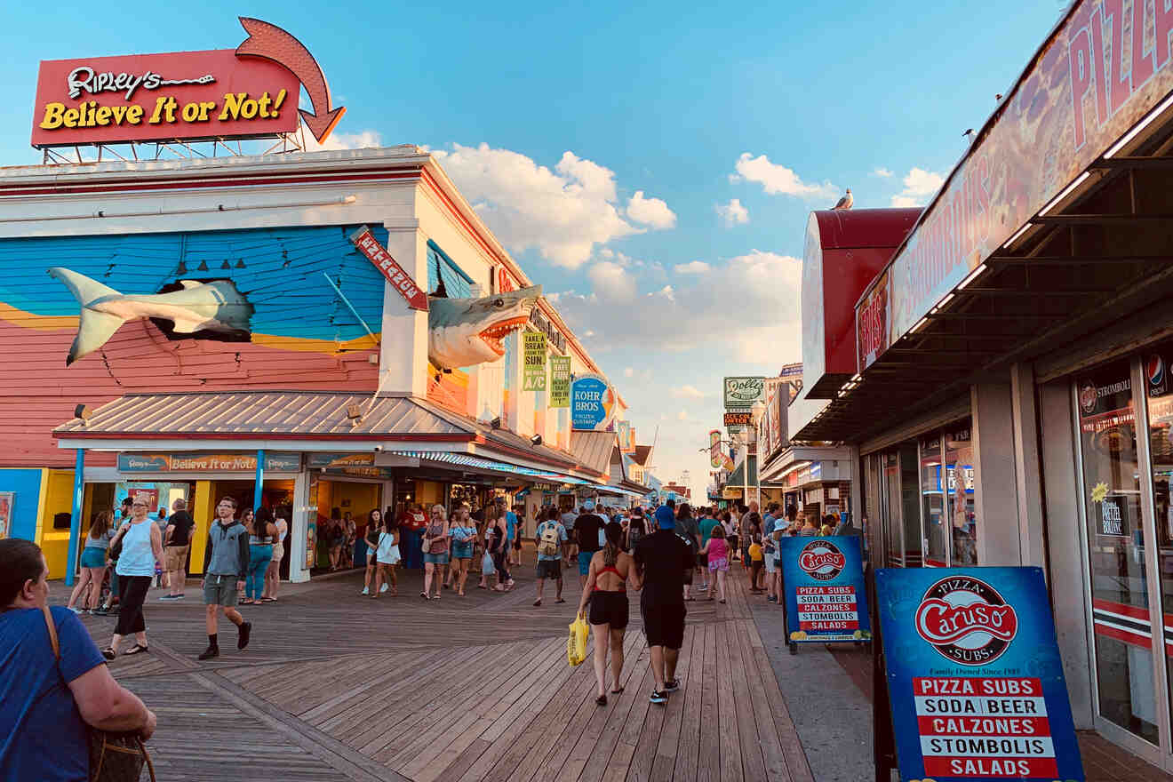 A bustling boardwalk featuring Ripley's Believe It or Not! and a pizza shop. People walk along the wooden path, enjoying a sunny day.