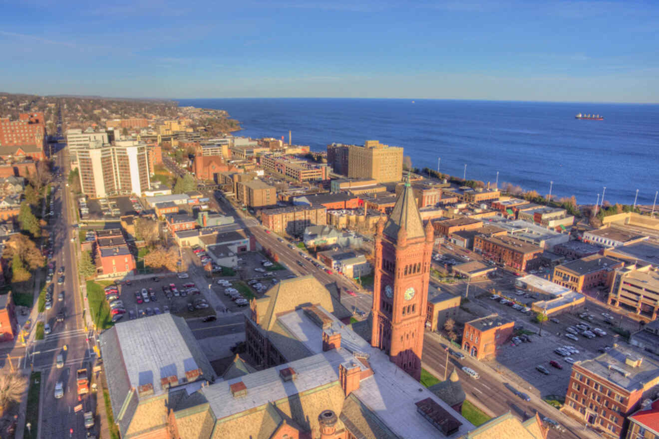 Aerial view of a lakeside city with a prominent clock tower, several buildings, and roads leading toward the water.