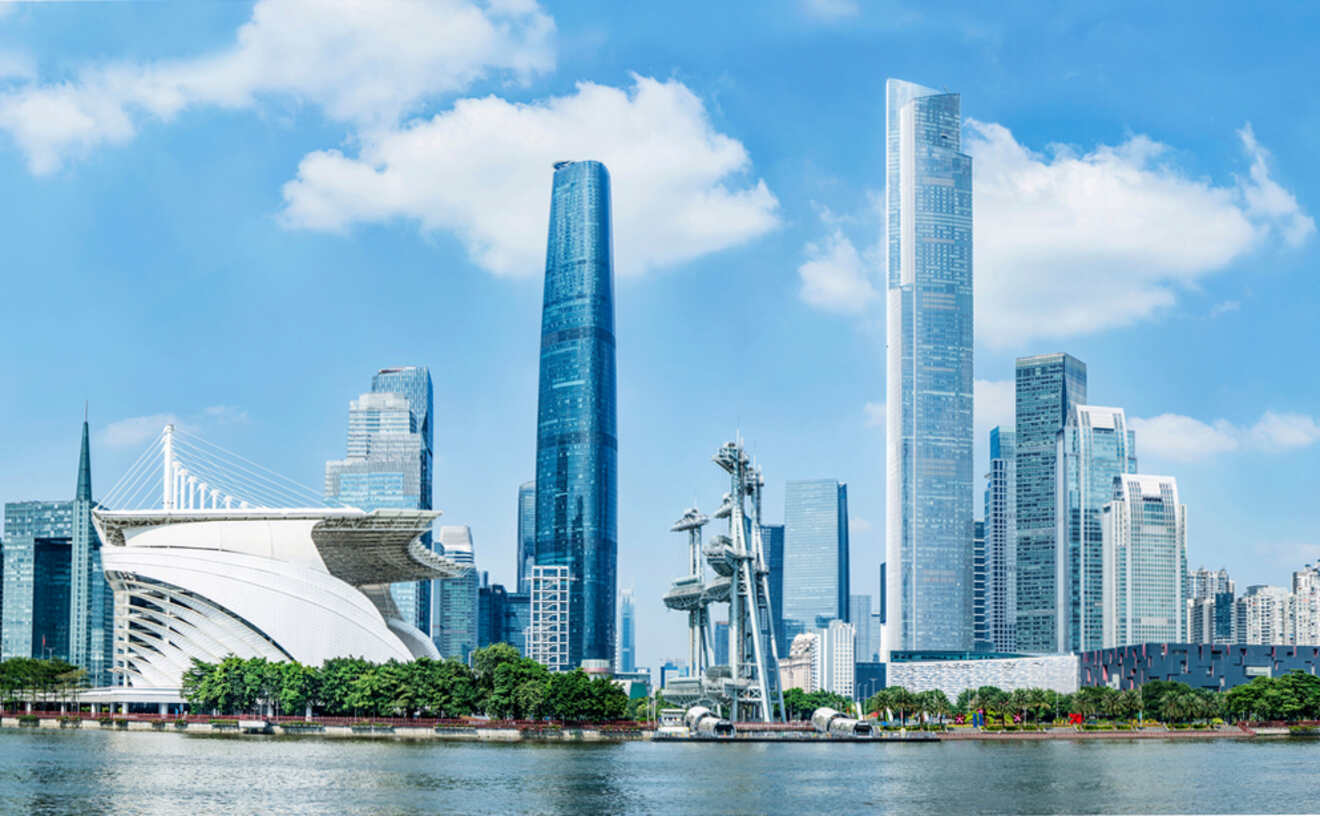 City skyline with modern skyscrapers and a distinctive white, curved architectural building on the waterfront under a blue sky.