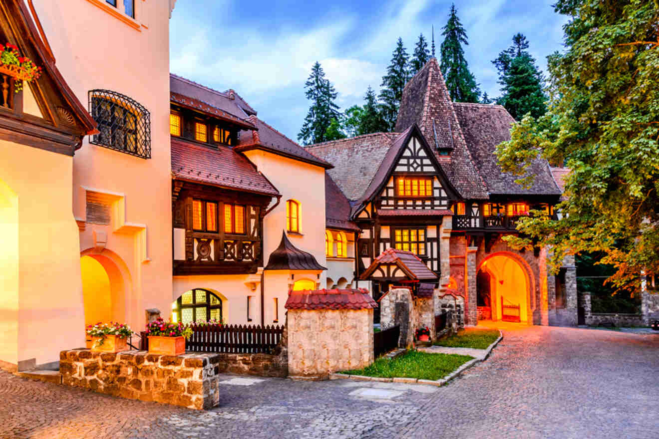 A picturesque European-style building with steep roofs and timber framing, surrounded by trees, glows warmly under twilight skies.