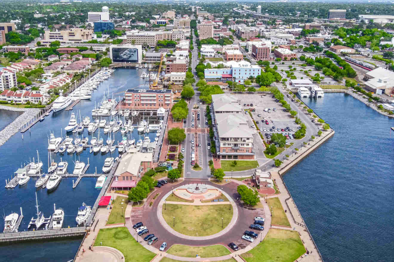 Aerial view of a cityscape featuring a marina with docked boats, surrounded by urban buildings and green spaces, near a waterfront area.