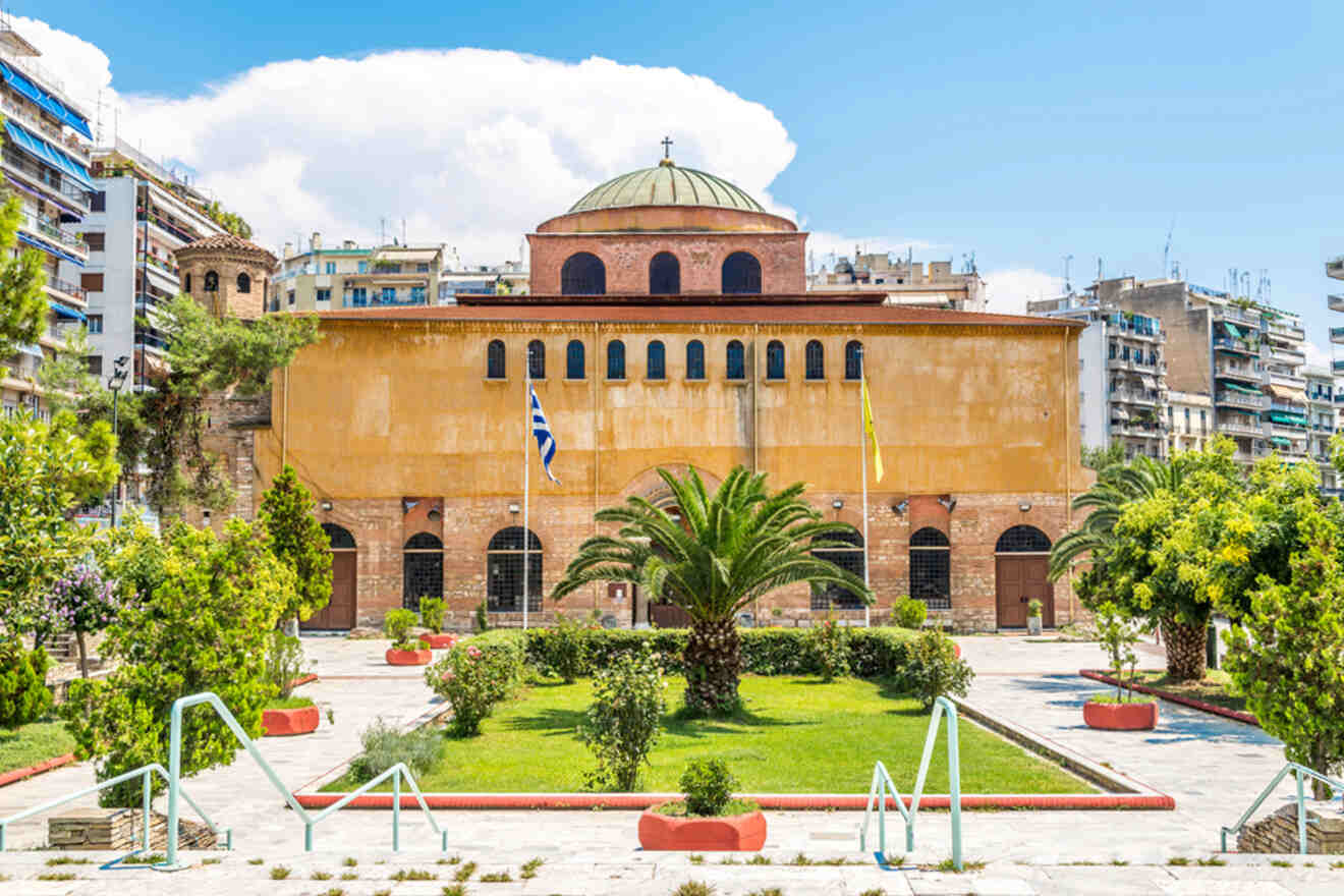 Historic building with a dome and arched windows, surrounded by trees and a garden, located in an urban area with residential buildings in the background.