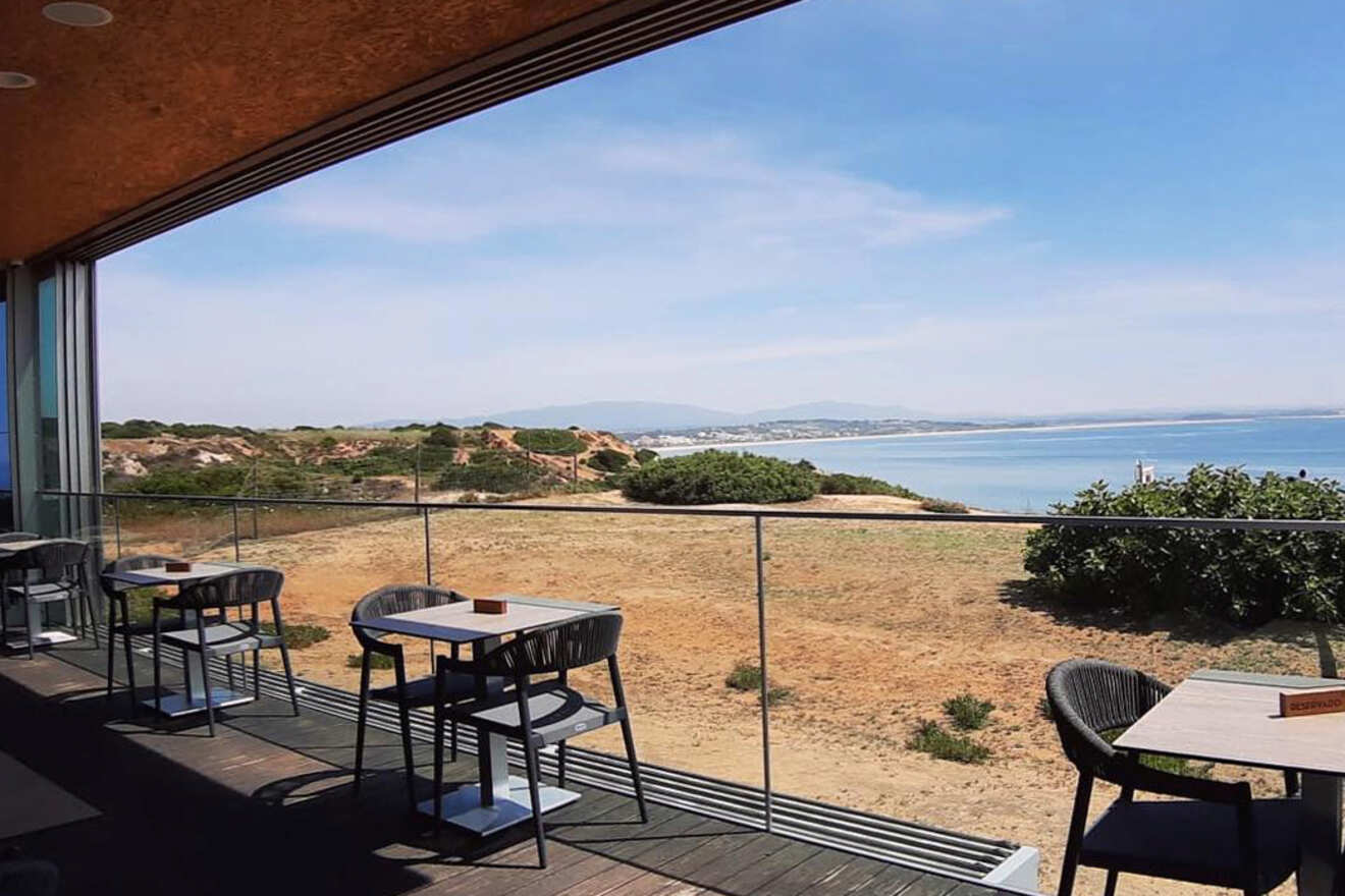 A seaside café with outdoor seating, overlooking a scenic coastline under a clear blue sky.